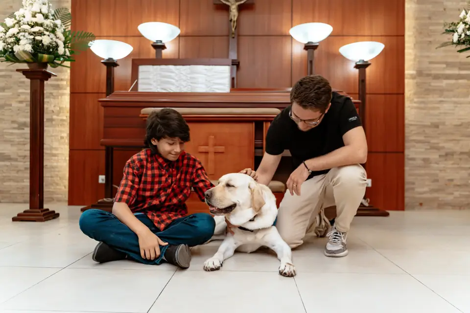 Niño y adulto acarician a un perro de canoterapia en una capilla