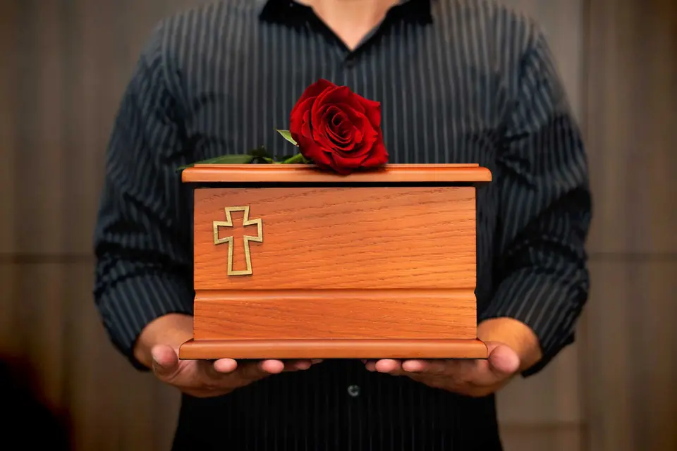Persona sostiene un cofre para cenizas con una rosa roja