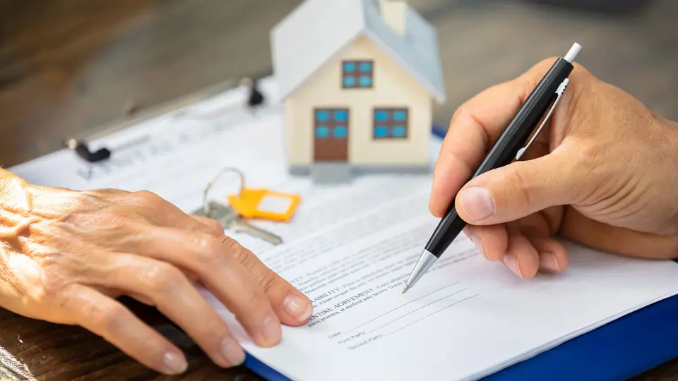 Firma de un título de propiedad junto a una maqueta de casa